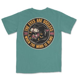 A traditional tattoo shirt featuring a panther with eyes in its mouth and the phrase “The eyes are useless when the mind is blind,” printed on a Comfort Colors tee for fans of tattoo art and alternative clothing.