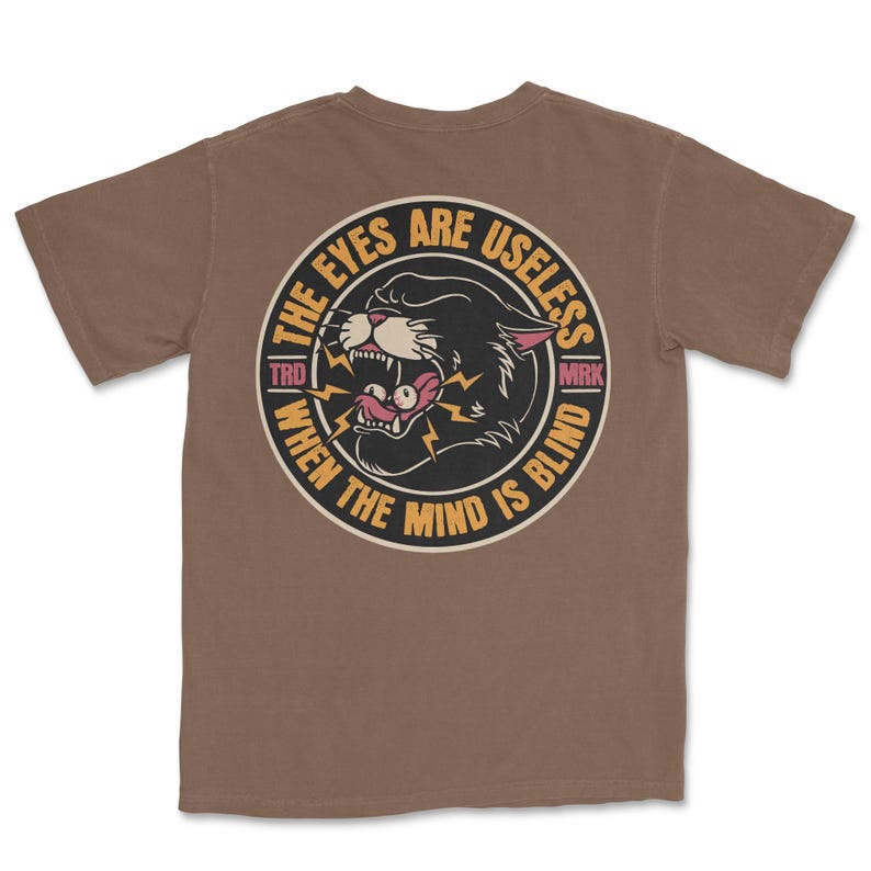 A traditional tattoo shirt featuring a panther with eyes in its mouth and the phrase “The eyes are useless when the mind is blind,” printed on a Comfort Colors tee for fans of tattoo art and alternative clothing.