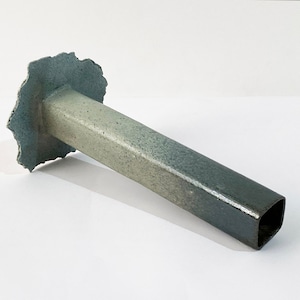 May include: A ceramic vase with a square opening and a light green to dark blue gradient. The top of the vase has a rough, irregular edge.