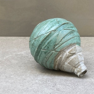 Puede incluir: Un jarrón de cerámica con un esmalte verde y blanco. El jarrón tiene un cuerpo redondeado y un cuello largo y estrecho.