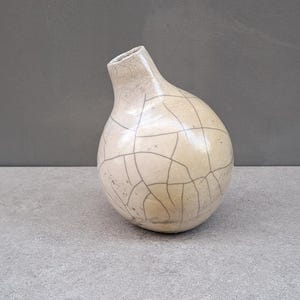 以下が含まれることがあります： ひび割れた釉薬を施した白い陶器の花瓶。花瓶は丸い胴体と細い首をしています。