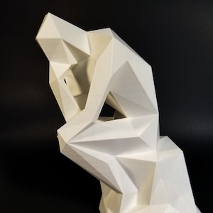 May include: A white geometric sculpture of a seated figure, reminiscent of Rodin's "The Thinker." The sculpture has a modern, angular design with sharp lines and facets. The figure is posed with its head resting on its hand.