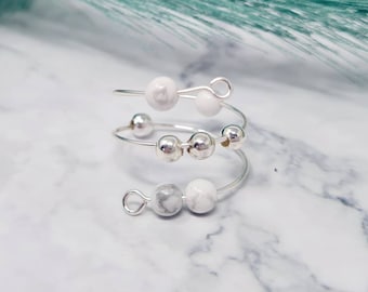 May include: A silver wire ring with white beads. The ring is made of three separate bands that are twisted together. The beads are white and have a marbled appearance.