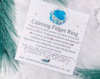 May include: A silver fidget ring with turquoise beads. The ring is adjustable and can be worn on any finger. The card reads "Calming Fidget Ring" and explains the benefits of fidgeting.  It also says "Wrap your new adjustable ring around your chosen finger for a comfortable fit. Be careful not to catch your ring on clothing as it may lose shape."