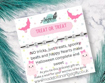 May include: A Halloween-themed bracelet with a black cord, pearl beads, and a heart charm. The card reads "TREAT OR TREAT" and includes text about Halloween and a website address. Pink bat and ghost illustrations decorate the card.