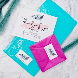May include: A pink and white tissue paper package with a thank you note that reads "Thank you for your support!" and a logo that says "Made for an Angel Designs". The note also includes a phone number and website address. The package is sitting on a blue bubble wrap envelope.