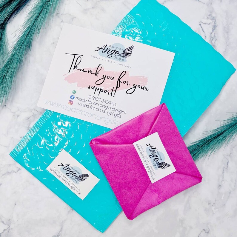 May include: A pink and white tissue paper package with a thank you note that reads "Thank you for your support!" and a logo that says "Made for an Angel Designs". The note also includes a phone number and website address. The package is sitting on a blue bubble wrap envelope.