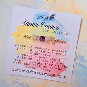 May include: A white card with a watercolour background and the text "Made for an Angel Super Power for anxiety". A bracelet with amethyst and moonstone beads is displayed on the card. The text on the card describes the benefits of the stones for anxiety.