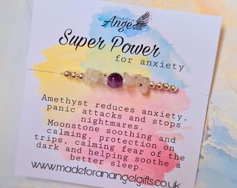May include: A white card with a watercolor background and the text "Made for an Angel Super Power for anxiety". A bracelet with amethyst and moonstone beads is displayed on the card. The text on the card describes the benefits of the stones for anxiety.