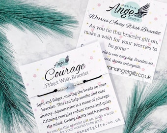 May include: A black string bracelet with silver beads and a light blue aquamarine bead. The bracelet is on a white card with the words "Courage Fidget Wish Bracelet" and a description of the bracelet's benefits. The card also includes the text "Made for an Angel Designs" and a website address.