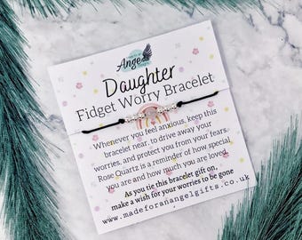 May include: A black string bracelet with silver-toned beads and a central rose quartz bead, attached to a white display card featuring the text "Daughter Fidget Worry Bracelet" and a printed rainbow graphic with floral accents.