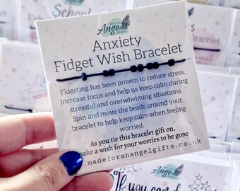 May include: A black string bracelet with small black beads attached to a white display card. The card features the text Anxiety Fidget Wish Bracelet, along with instructions on how to use the beads to reduce stress and make a wish when tying it on.