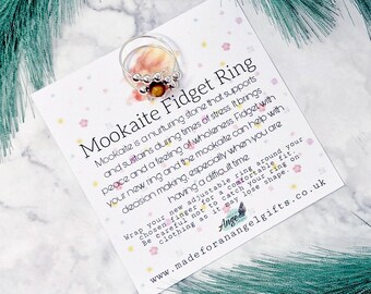 May include: Silver ring with a brown mookaite stone and silver beads. The ring is adjustable and can be worn on any finger. The card reads "Mookaite Fidget Ring" and explains the benefits of mookaite. The text on the card reads "Mookaite is a nurturing stone that supports and sustains during times of stress. It brings peace and a feeling of wholeness. Fidget with your new ring and the mookaite can help with decision making, especially when you are having a difficult time. Wrap your new adjustable ring around your chosen finger for a comfortable fit. Be careful not to catch your ring on clothing as it may lose shape. www.madeforanangelgifts.co.uk"