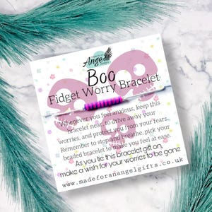 May include: Pink and white bracelet with a pink and purple striped band. The bracelet is on a card with the text "Boo Fidget Worry Bracelet" and instructions on how to use it.  "Whenever you feel anxious, keep this bracelet near, to drive away your worries, and protect you from your fears. Remember to stop and breathe, pick your beaded bracelet to make you feel at ease. As you tie this bracelet gift on, make a wish for your worries to be gone www.madeforanangelgifts.co.uk"