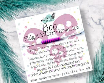 May include: Pink and white bracelet with a pink and purple striped band. The bracelet is on a card with the text "Boo Fidget Worry Bracelet" and instructions on how to use it.  "Whenever you feel anxious, keep this bracelet near, to drive away your worries, and protect you from your fears. Remember to stop and breathe, pick your beaded bracelet to make you feel at ease. As you tie this bracelet gift on, make a wish for your worries to be gone www.madeforanangelgifts.co.uk"
