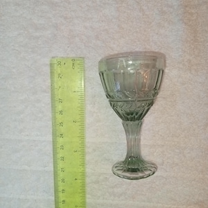 Puede incluir: Una copa de vidrio verde transparente con un diseño facetado. La copa tiene un tallo alto y una base ancha.