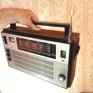 Könnte beinhalten: Vintage Holzradio mit silberner Front und schwarzem Griff. Das Radio hat ein Einstellrad, einen Lautsprechergrill und eine ausziehbare Antenne. Der Text "OKEAH-214" ist sichtbar. Ein Retro-Elektronikgerät.