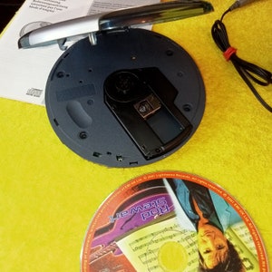 May include: A black portable CD player with the lid open, revealing the CD slot. A CD with a colorful design is visible in the background. The CD features the text "Rod Stewart" and the text "2001 EMI UK Ltd. All rights reserved."