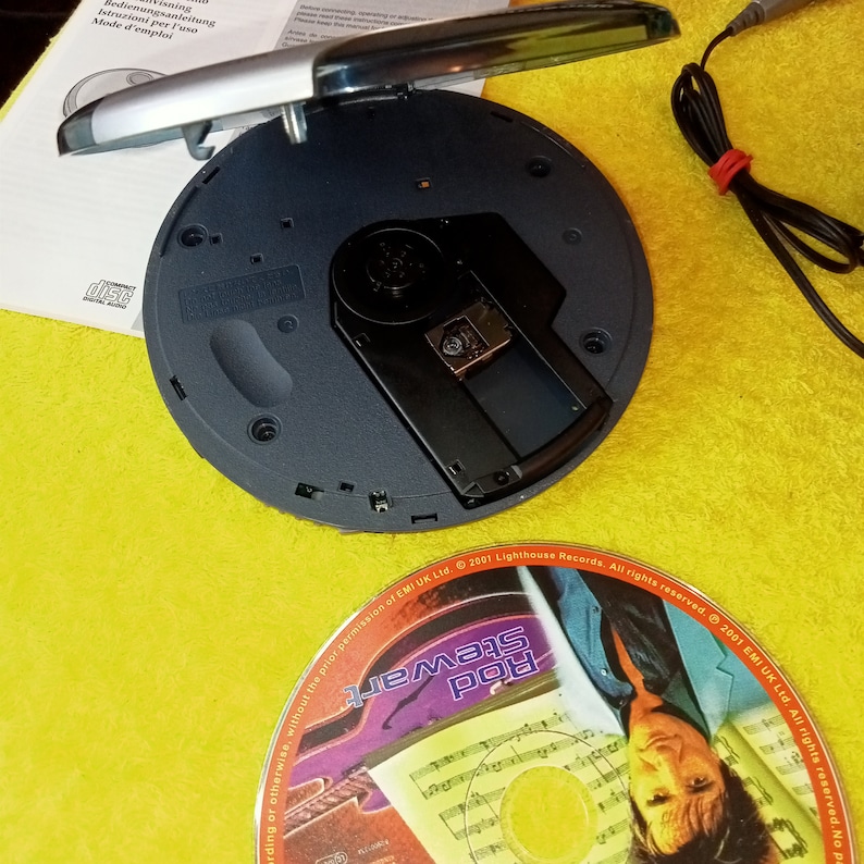 May include: A black portable CD player with the lid open, revealing the CD slot. A CD with a colorful design is visible in the background. The CD features the text "Rod Stewart" and the text "2001 EMI UK Ltd. All rights reserved."