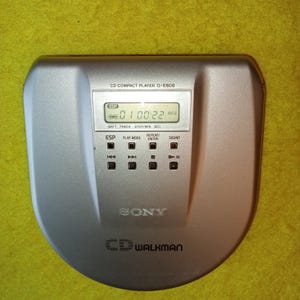 May include: A silver Sony CD Walkman D-E808 compact disc player with a digital display showing "0100:22 AVLS". The player has buttons for ESP, play mode, repeat, enter, and sound.
