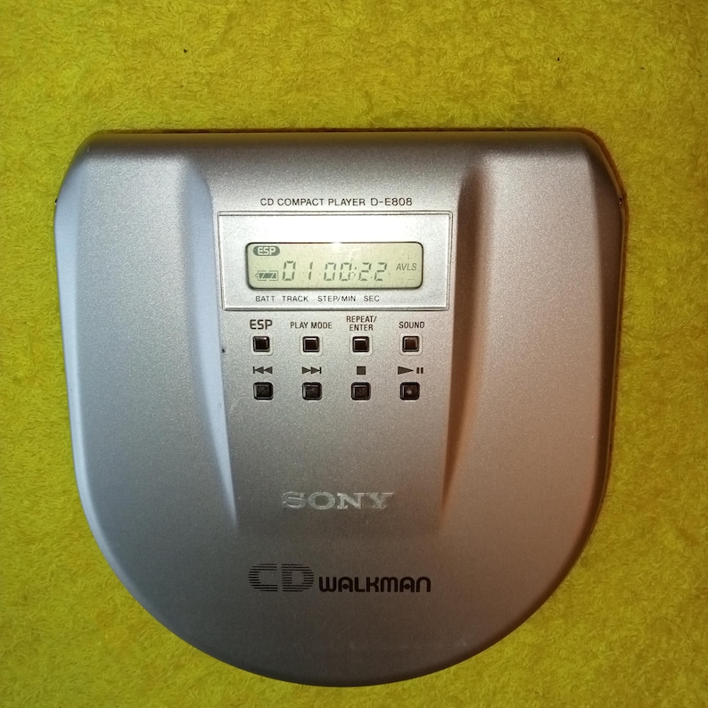 May include: A silver Sony CD Walkman D-E808 compact disc player with a digital display showing "0100:22 AVLS". The player has buttons for ESP, play mode, repeat, enter, and sound.
