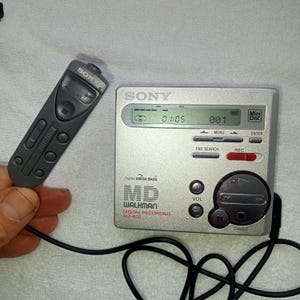 Könnte beinhalten: Ein silbernes Sony MD Walkman Digital-Aufnahmegerät mit Fernbedienung. Das Gerät zeigt "01:05" und "001" auf dem Bildschirm an. Auf dem Gerät sind die Wörter "Digital MEGA BASS" und "WALKMAN" aufgedruckt.