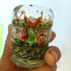 Op de afbeelding: Een helder, decoratief glazen object met rode en witte rozen en groene bladeren erin. Het glas heeft een facetgeslepen bovenkant en een decoratieve basis. De rozen zijn zo gerangschikt dat ze in een vaas lijken te staan.