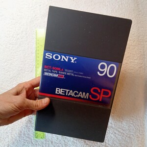 May include: A black Sony Betacam SP video cassette with the text "BCT-90MLA METAL TAPE/BANDE METAL" and "BETACAM SP" printed on the label. The cassette is 90 minutes long.