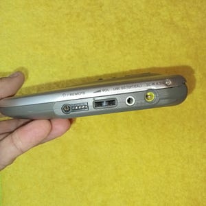 May include: A silver-colored portable CD player with a volume knob, remote control input, line out, optical out, and DC in 4.5V ports.