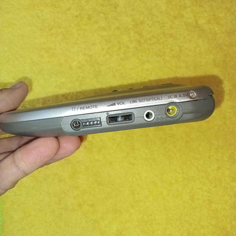 May include: A silver-colored portable CD player with a volume knob, remote control input, line out, optical out, and DC in 4.5V ports.