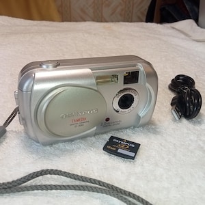 Cámara digital compacta Olympus CAMEDIA D-390 estilo retro en funcionamiento, color plata, probada con tarjeta de memoria, decoración retro.