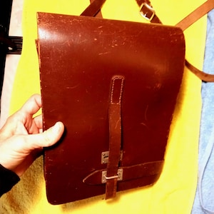 May include: A brown leather satchel with a flap closure and adjustable shoulder strap. The bag features a rectangular shape with a buckle closure and a smaller strap detail. The leather has a worn appearance.