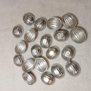 以下が含まれることがあります： 銀色の楕円形の型が複数個写っています。各型はリブ模様で、上部に小さな円形のくぼみがあります。明るい色の表面に散らばっており、調理に関連するテーマを示唆しています。
