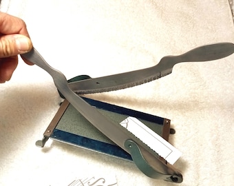 May include: A vintage metal violin bridge cutter with a serrated blade. The cutter has a dark metal finish and a wooden base. The handle is held by a hand. A small piece of paper is attached to the base.