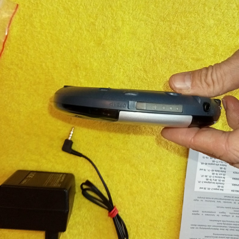 May include: A blue and silver portable CD player with a headphone jack and a power adapter. The player has a display screen and buttons for controlling playback.