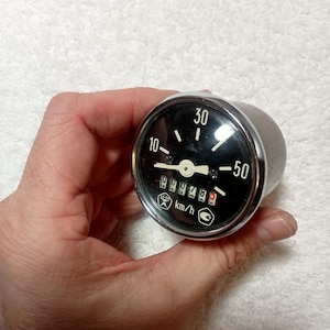 Op de afbeelding: Een verchroomde snelheidsmeter met een zwart gezicht en witte markeringen. De snelheidsmeter geeft tot 50 km/h aan en heeft een digitale kilometerteller die 144474 aangeeft.