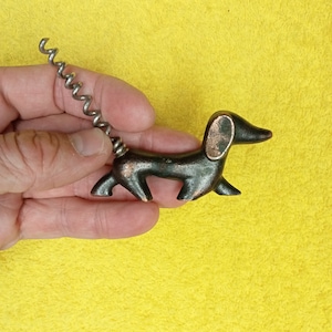 Può includere: Un cavatappi a forma di bassotto con finitura bronzo scuro. Le orecchie e il corpo del cane hanno un accento color rame. Il cavatappi è realizzato in metallo color argento ed è attaccato alla schiena del cane.