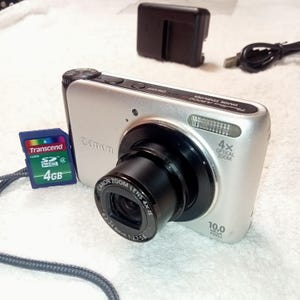 May include: Silver Canon digital camera with a black lens and a 4x optical zoom. Includes a 4GB SD card and a charger. The camera has a 10.0 megapixel resolution.