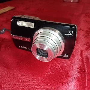 May include: A black Olympus digital camera with a silver lens. The camera has a 7.1 megapixel resolution and a 5x optical zoom.