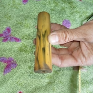 Könnte beinhalten: Ein gelber und schwarzer, gemusterter Holzstift mit einem Loch in der Mitte.