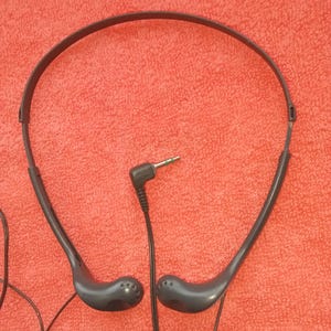 Könnte beinhalten: Dunkelgrauer Sony-Kopfhörer mit Bügel und Ohrhörern, verbunden durch ein schwarzes Kabel mit einem 3,5-mm-Klinkenstecker. Der Kopfhörer befindet sich vor einem roten Hintergrund.