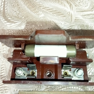May include: A brown ceramic fuse holder with two metal terminals and a white ceramic fuse inside.