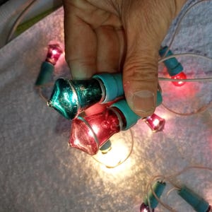 May include: A string of vintage Christmas lights with clear bulbs and coloured glass covers. The bulbs are red, green, and blue. The lights are strung together with white wire.