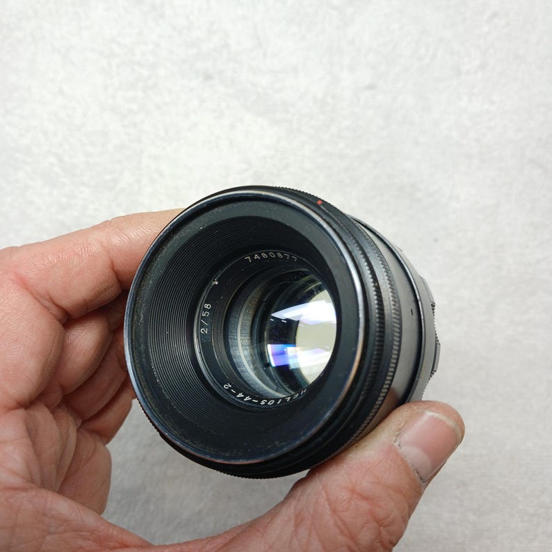 Peut inclure: Un objectif d'appareil photo noir avec des d&eacute;tails argent&eacute;s, tenu dans une main. L'objectif porte des inscriptions, dont "2/58" et "HELIOS-44-2". Le verre refl&egrave;te la lumi&egrave;re, et l'objectif est net. Accessoire de photographie.