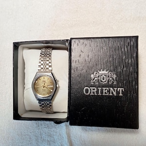 May include: A set of three ceramic mugs with a speckled, matte finish. The mugs are in shades of cream, light brown, and dark brown. Each mug has a simple, minimalist design and a rounded handle.