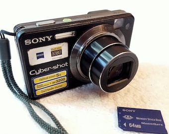 Sony Cybershot DSC-W150 negra en funcionamiento, cámara de 8,1 MP, zoom óptico de 5x, cámara digital de principios de la década de 2000, algunos rayones menores en la lente
