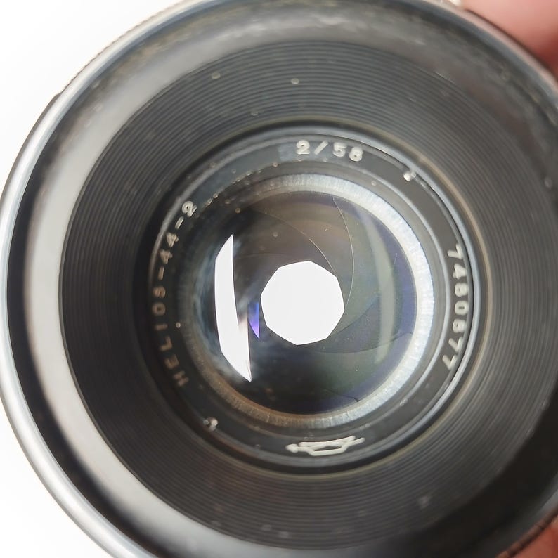 Peut inclure: Gros plan sur un objectif d'appareil photo noir Helios-44-2 avec une ouverture argent&eacute;e. L'objectif porte les inscriptions "2/58" et "7460677". Les lamelles de l'ouverture forment une forme polygonale. L'objectif est con&ccedil;u pour la photographie.