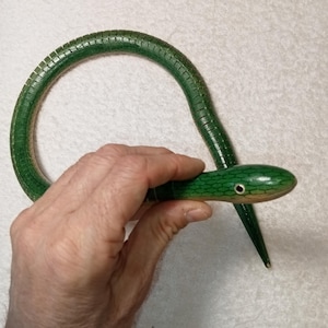 Op de afbeelding: Een groen houten slangen speelgoed met een getextureerd oppervlak en een geschilderd oog. De slang is in een cirkelvorm gekruld.