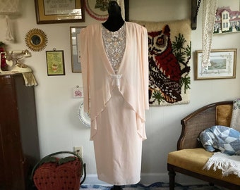 Puede incluir: Un vestido rosa pálido con una superposición de encaje y una chaqueta a juego. El vestido tiene un corpiño ajustado y una falda fluida. La chaqueta tiene un dobladillo con volantes y un lazo en el escote. El vestido se muestra en un maniquí sobre un fondo blanco.