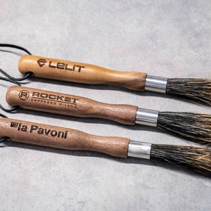May include: Three wooden-handled cleaning brushes with black leather straps. The brushes are labelled "Lelit", "Rocket Espresso Milano", and "La Pavoni".